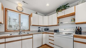 A compact kitchen with white cabinets, a microwave, a stove, and a sink. - Ocean-view home with pool, private hot tub, W/D - near the beach (Avon)
