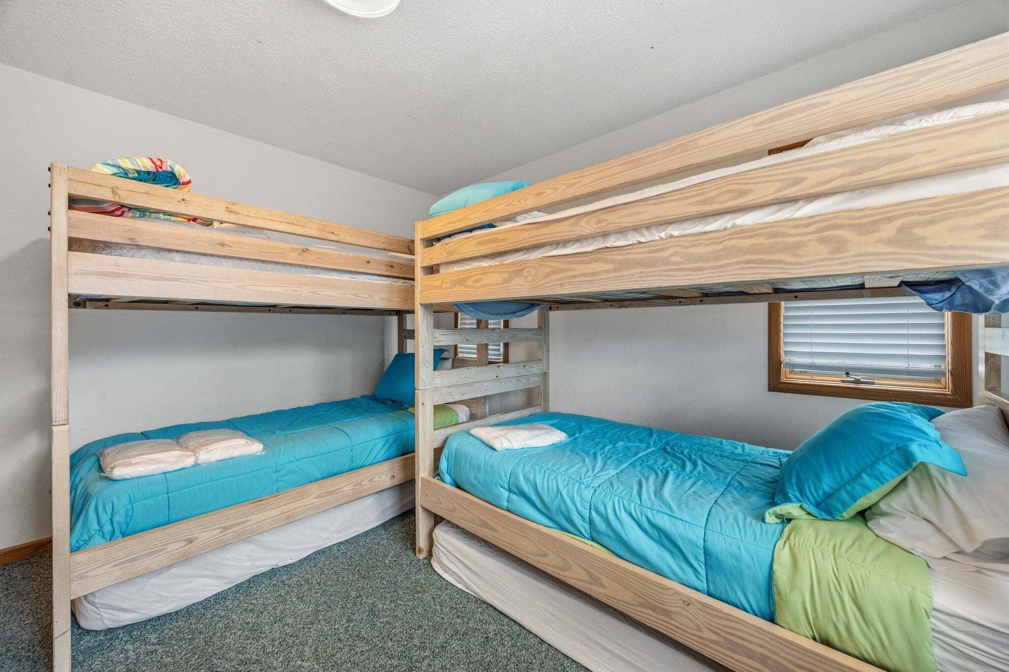 A room with bunk beds, a window with blinds, and a carpeted floor.