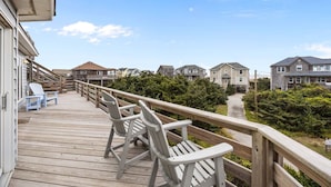 A wooden deck with chairs, a pathway leading to houses, and a clear sky. - Ocean-view home with pool, private hot tub, W/D - near the beach (Avon)