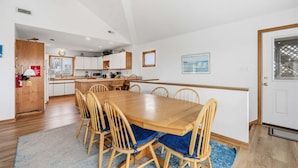 A dining area with a wooden table and chairs, a kitchen in the background, and a door with a window. - Ocean-view home with pool, private hot tub, W/D - near the beach (Avon)