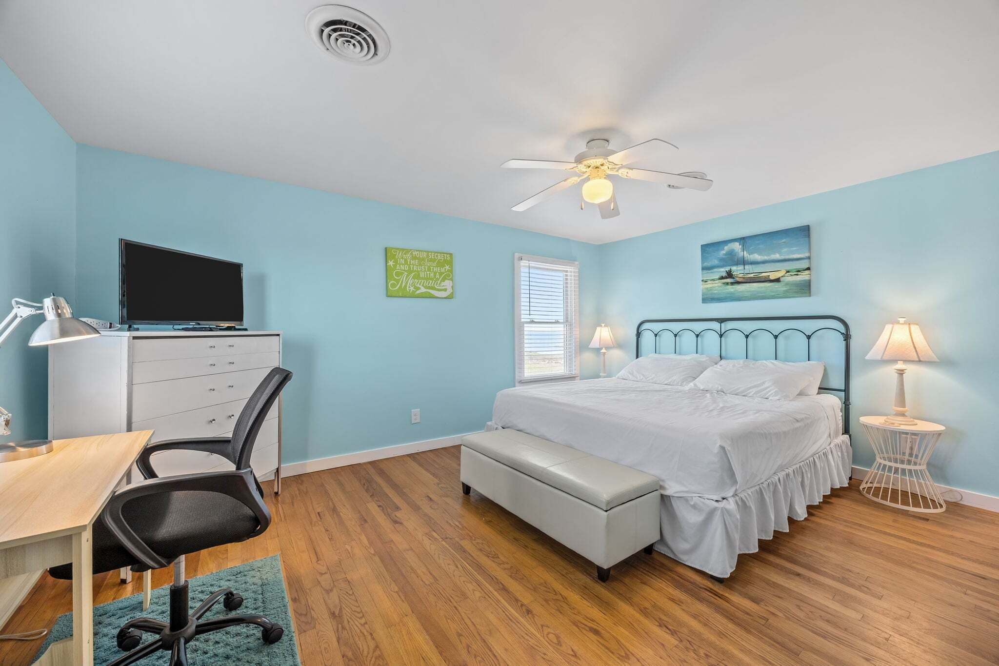 A bedroom with a bed, desk, chair, and a ceiling fan.