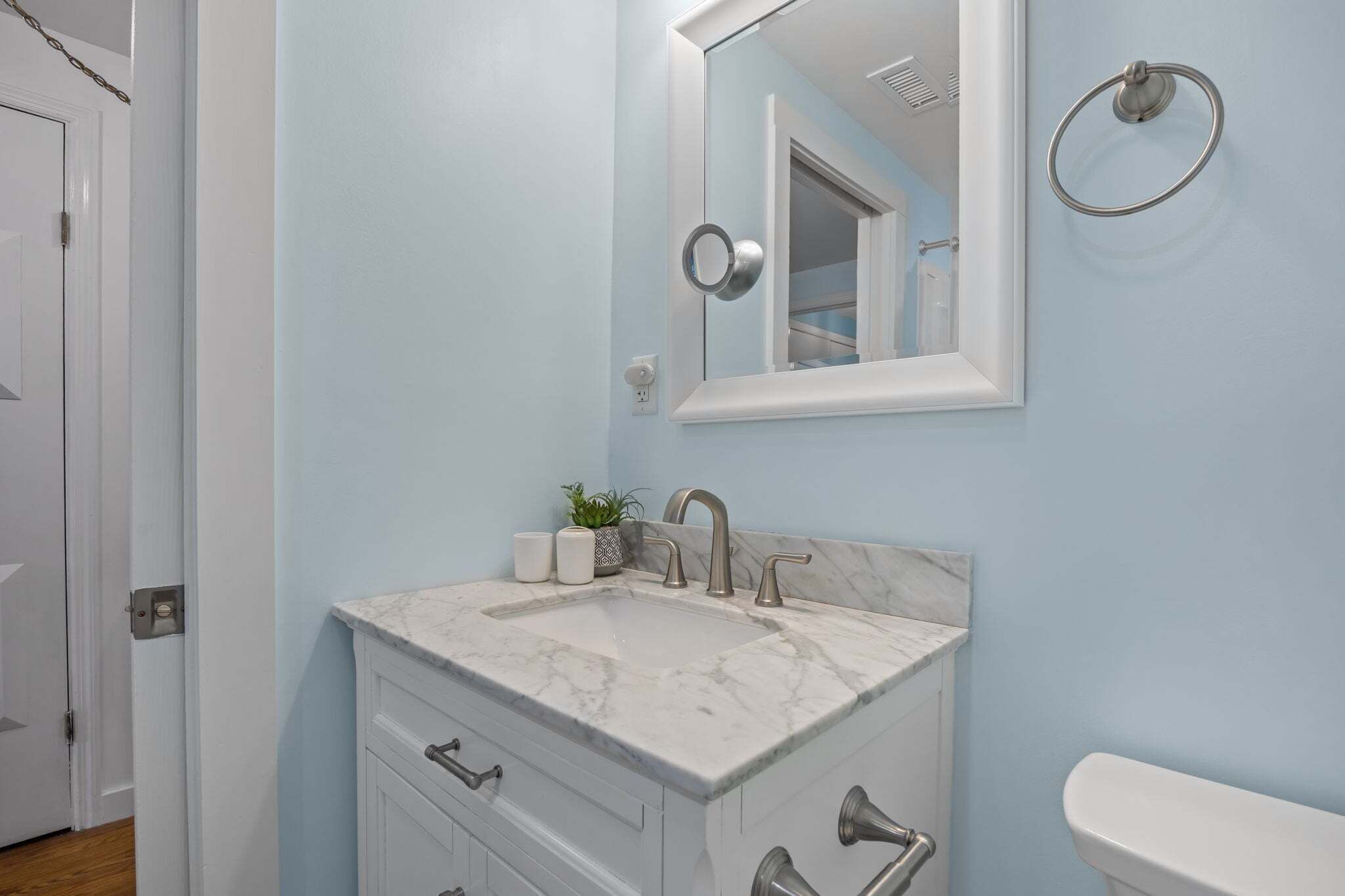 A bathroom with a marble sink, a mirror, a towel ring, and a toilet.