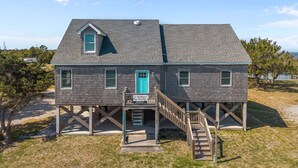 A two-story wooden house with a balcony, a blue door, and a staircase leading to the deck. - Waterfront house w/water views, private hot tub, theater room, game room/bar, AC (Frisco)