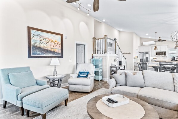 A spacious living room with a large sofa, a chair, and a coffee table. There is a staircase leading to an upper level.
