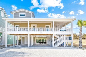 A two-story beach house with a covered porch, a balcony, and a rental sign.
