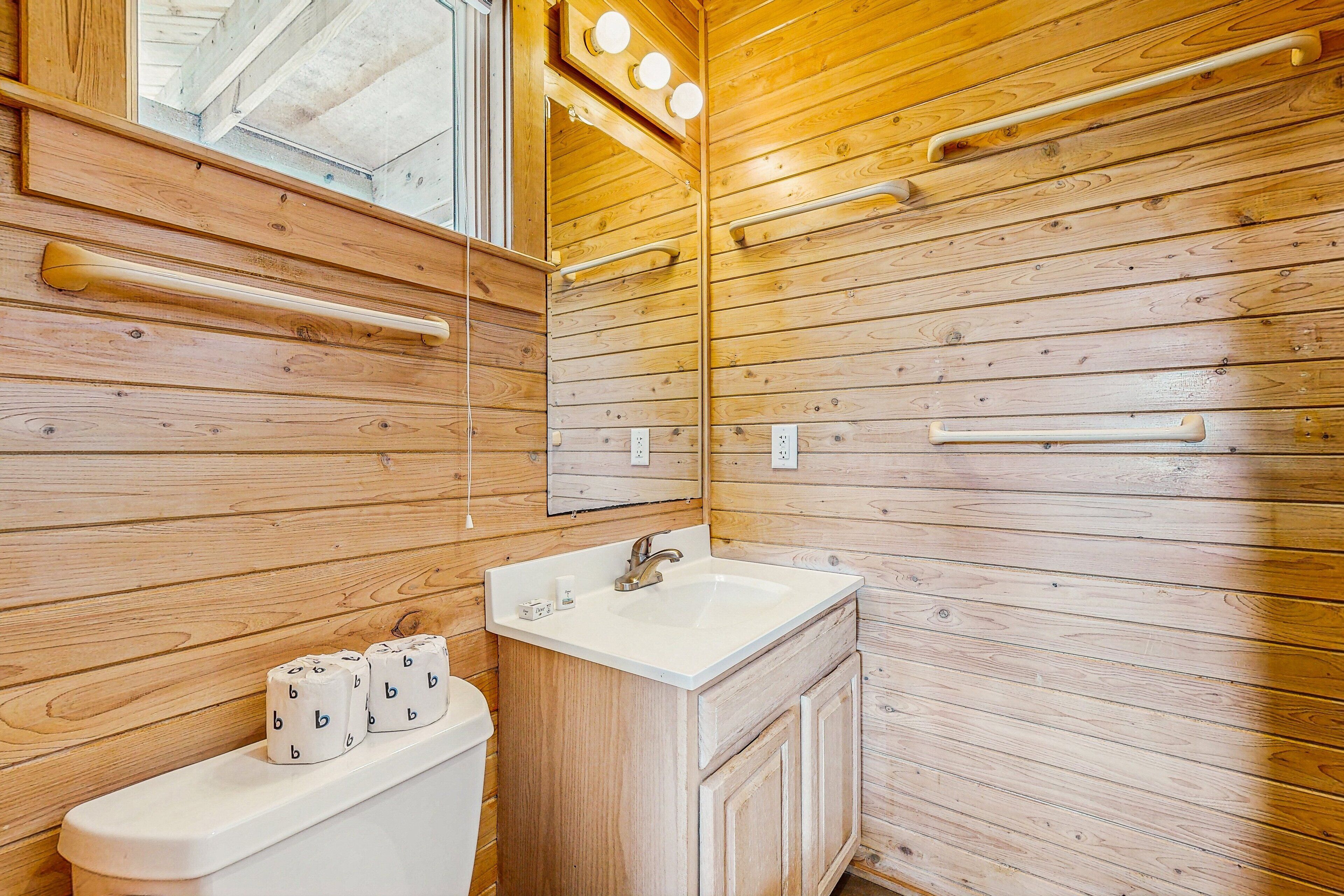 Un baño con paneles de madera, un lavamanos blanco, un espejo y tres rollos de papel higiénico.