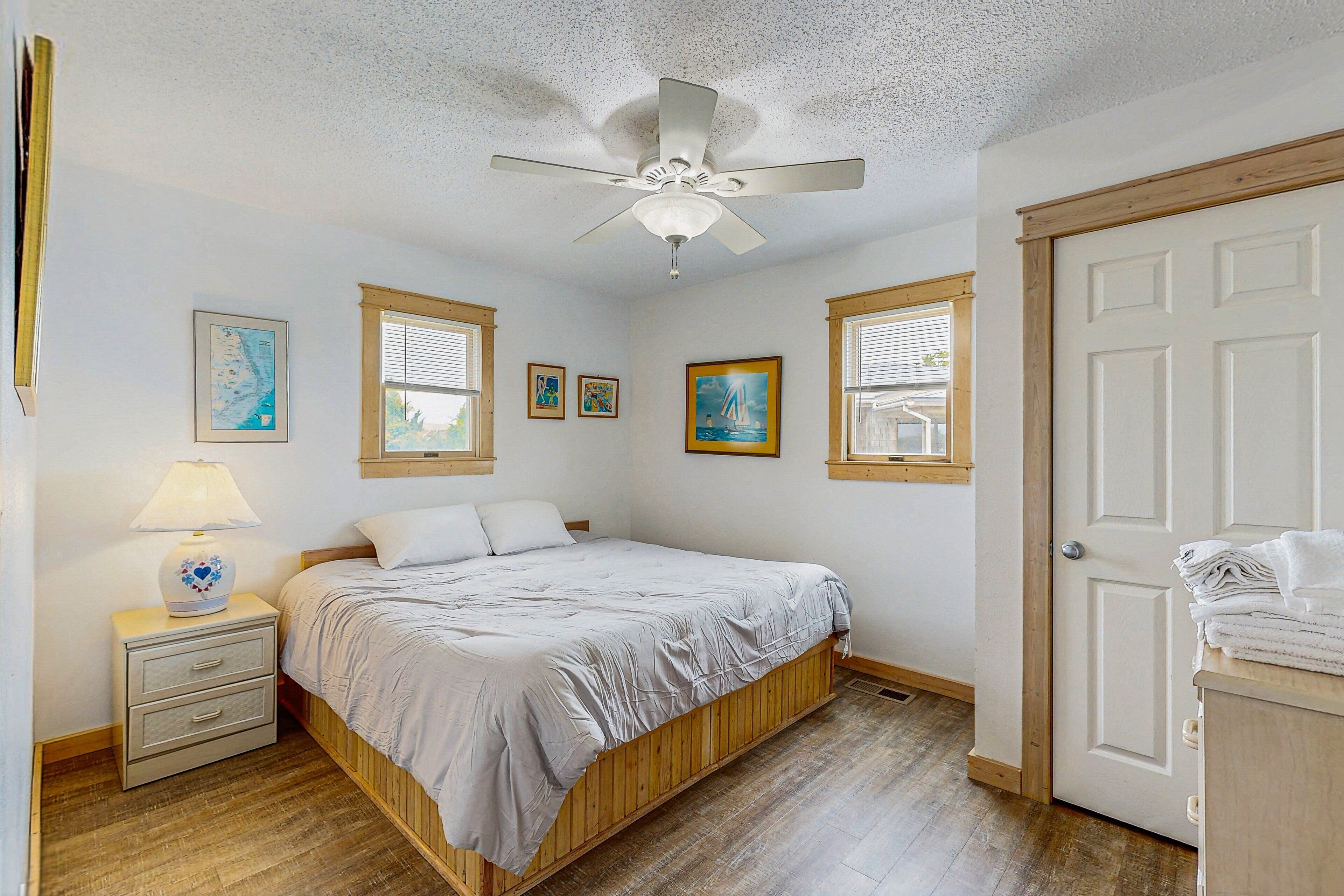 A bedroom with a bed, a nightstand, a ceiling fan, and a door.
