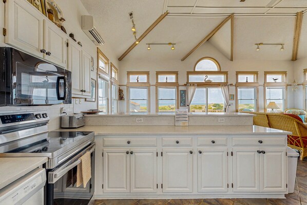 A spacious kitchen with white cabinetry, stainless steel appliances, and large windows offering views of the outdoors.