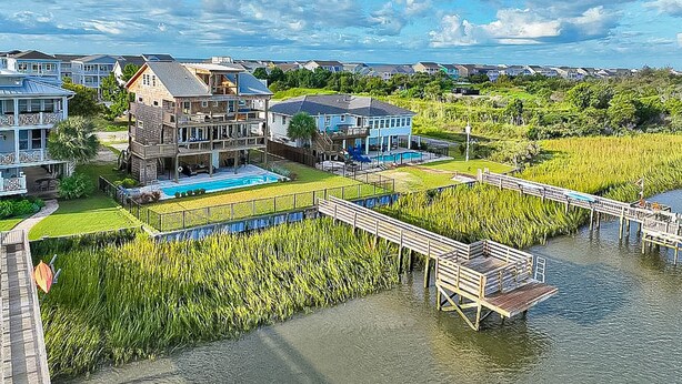 A coastal residential area with houses, a dock, and a swimming pool. - Intracoastal Indulgence: Waterfront, pool, dock and water views! (Holden Beach)