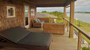 A wooden deck with a bed, two wicker chairs, and a view of a lake. - Intracoastal Indulgence: Waterfront, pool, dock and water views! (Holden Beach)