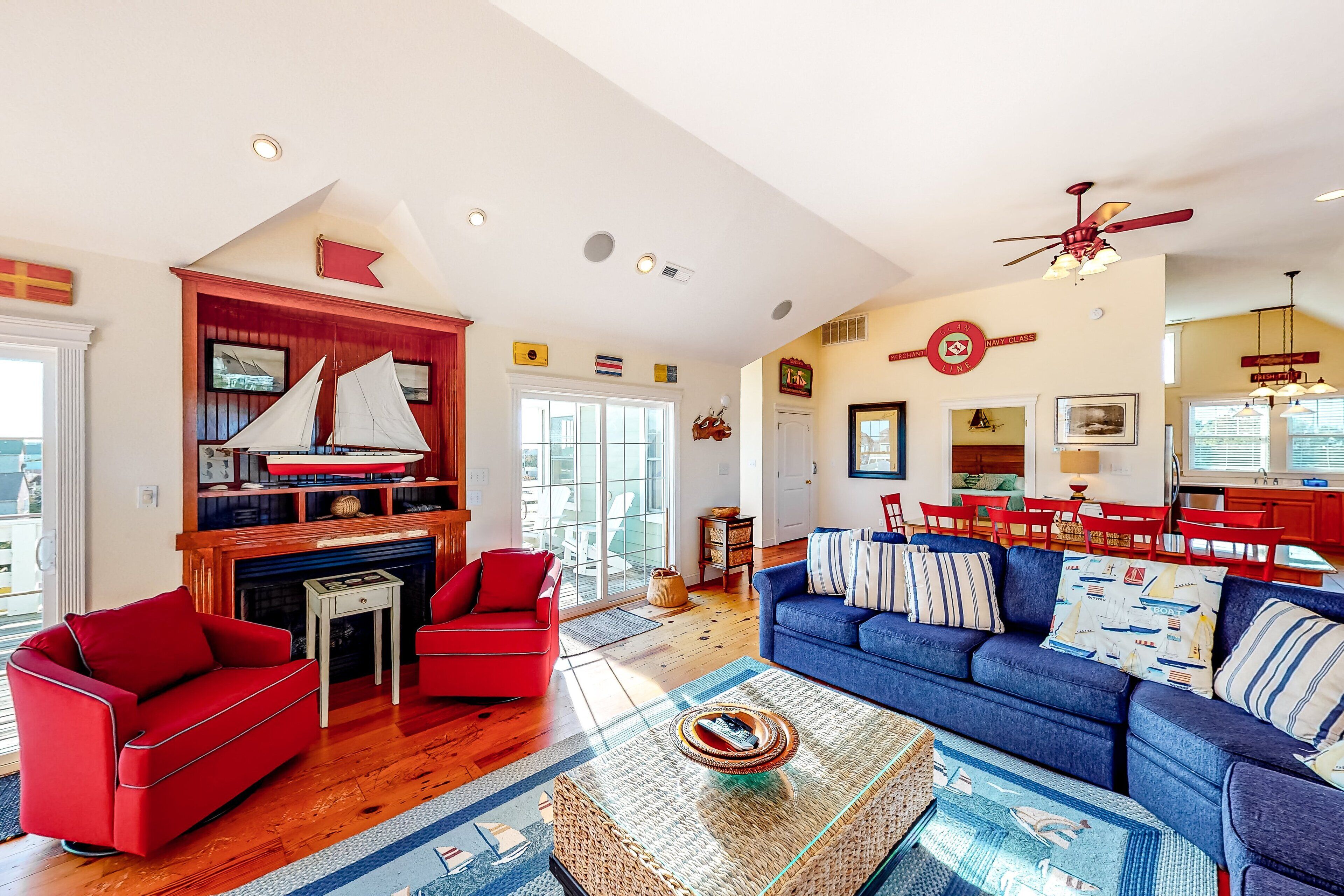 A spacious living room with a fireplace, red and blue sofas, wooden floors, and a large window.