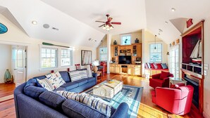 A spacious living room with a large sofa, a red armchair, and a wooden coffee table. There is a kitchen area with wooden cabinets and a television. - Beautiful house with private pool, hot tub, central AC, & washer/dryer (Salvo)