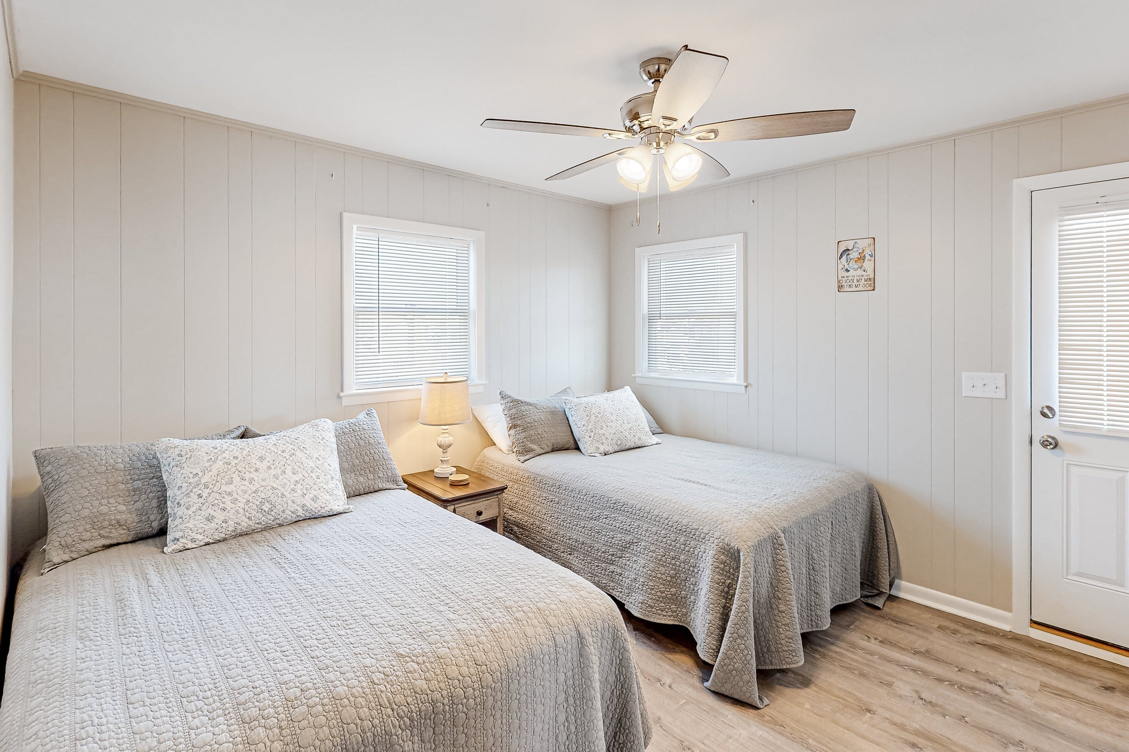 Une chambre avec deux lits, un ventilateur de plafond et une porte avec une fenêtre.