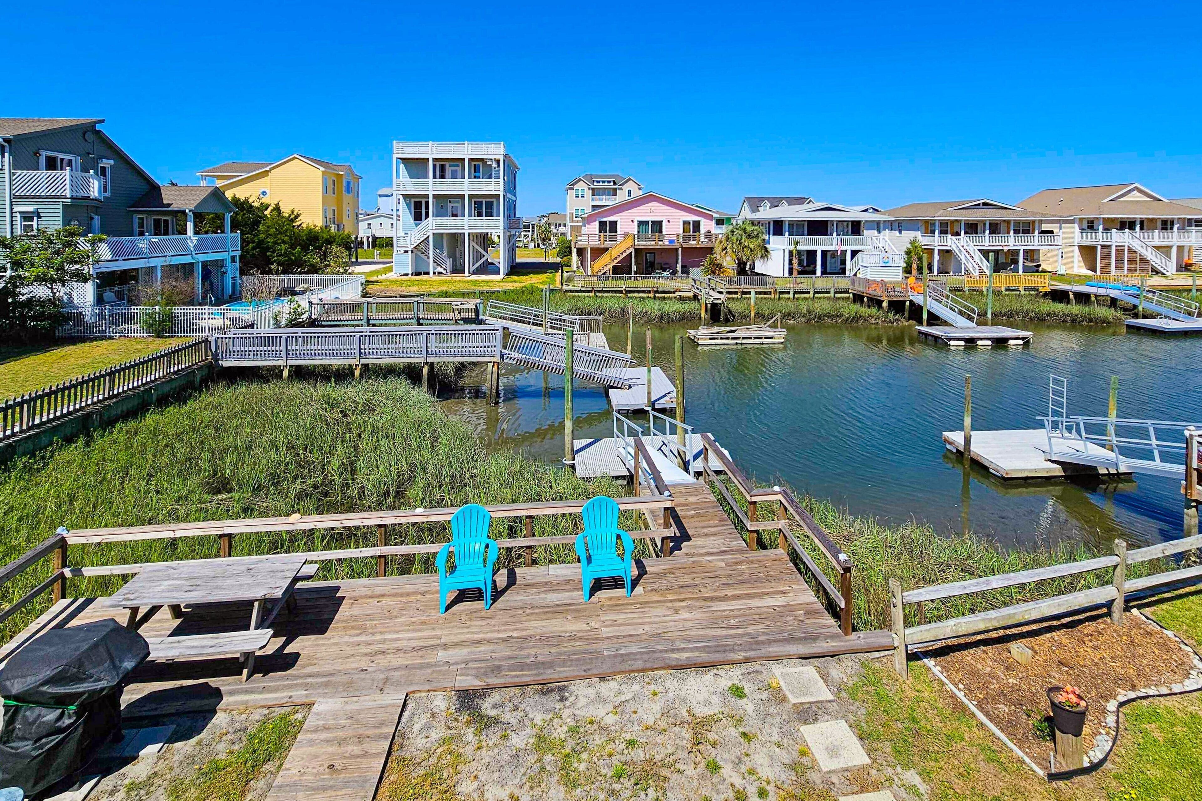 A waterfront property with a wooden deck, two blue chairs, and a dock extending into the water.