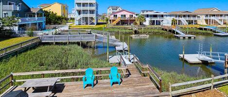 A waterfront property with a wooden deck, two blue chairs, and a dock extending into the water.