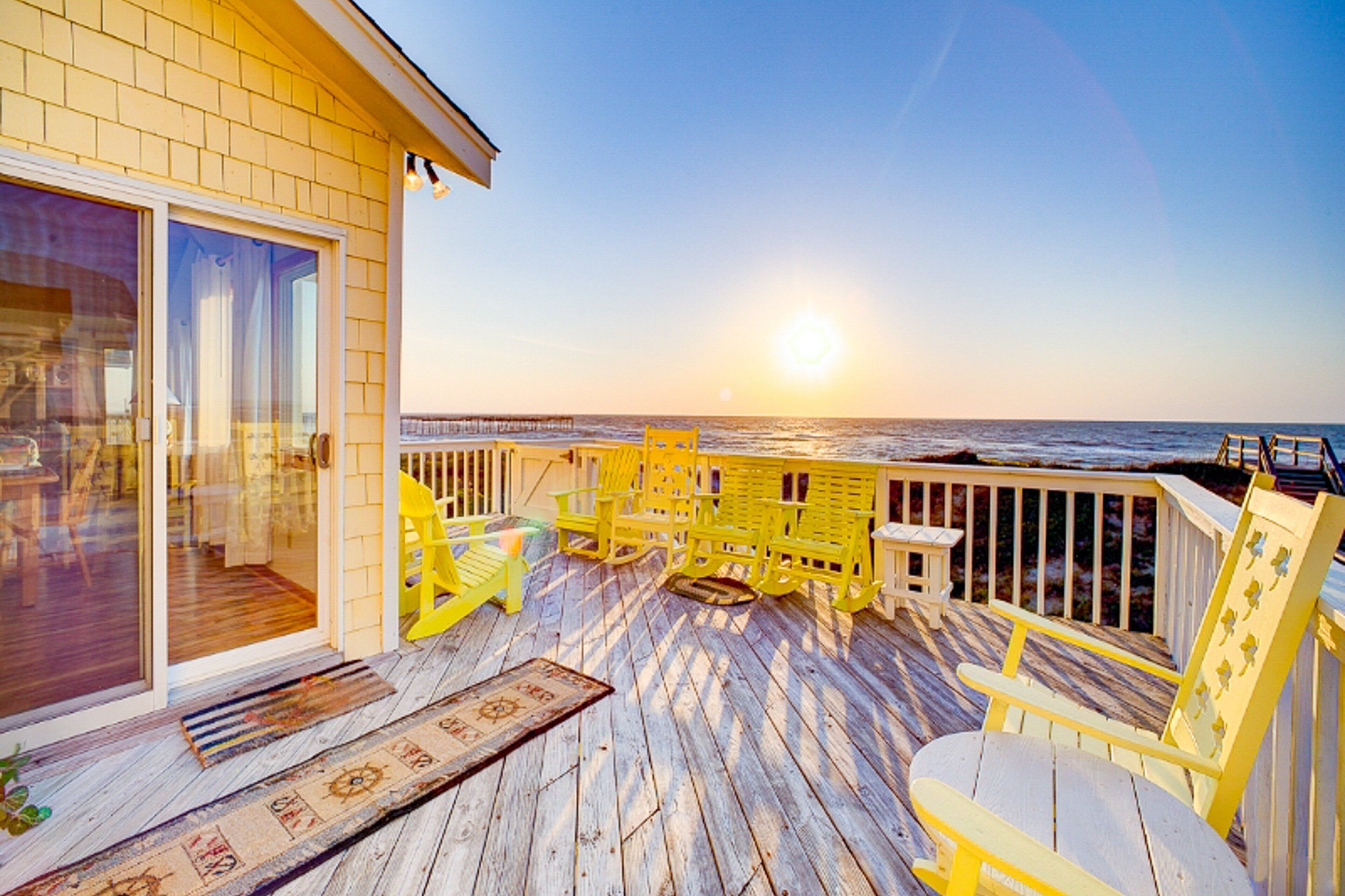 A wooden deck with yellow chairs and a table, overlooking the ocean.