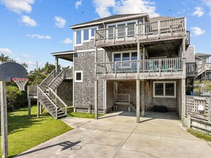 A multi-level wooden house with a basketball hoop, outdoor stairs, and a fenced yard.