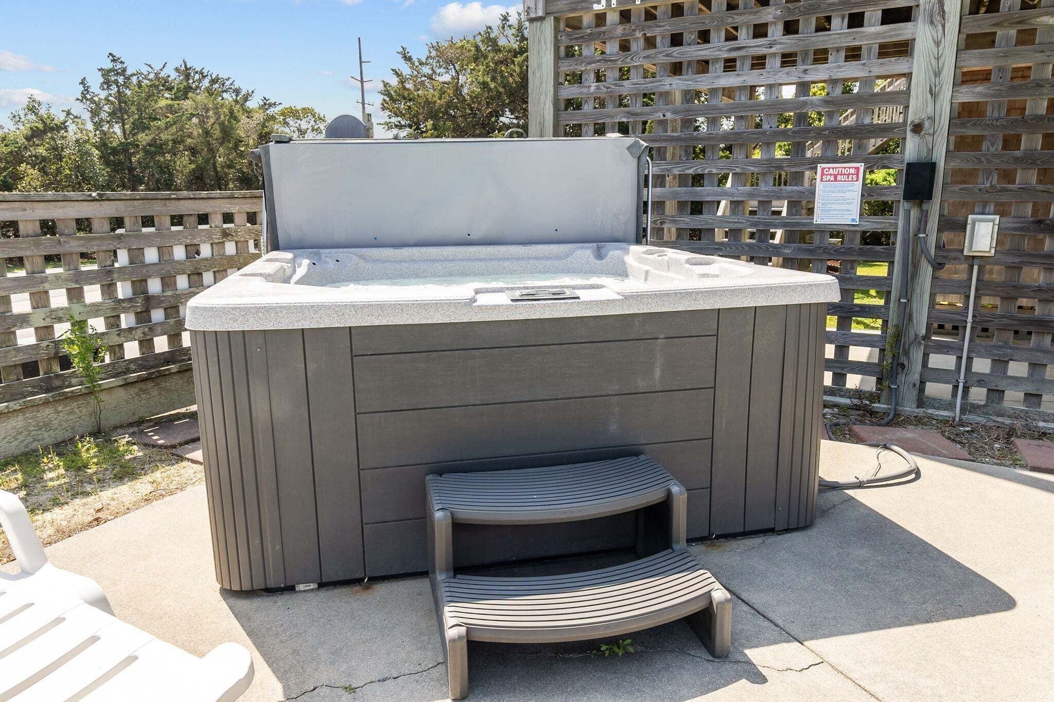 A hot tub with a wooden step leading up to it, a wooden fence in the background, and a sign indicating spa rules.