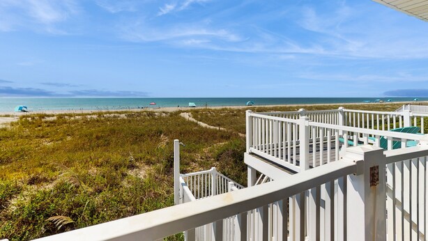 A beach view from a white wooden deck with a railing, overlooking the ocean and beach area.
