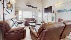 A spacious living room with leather sofas, a flat-screen TV, and nautical decor including a fish sculpture and a fish-shaped wall hanging.