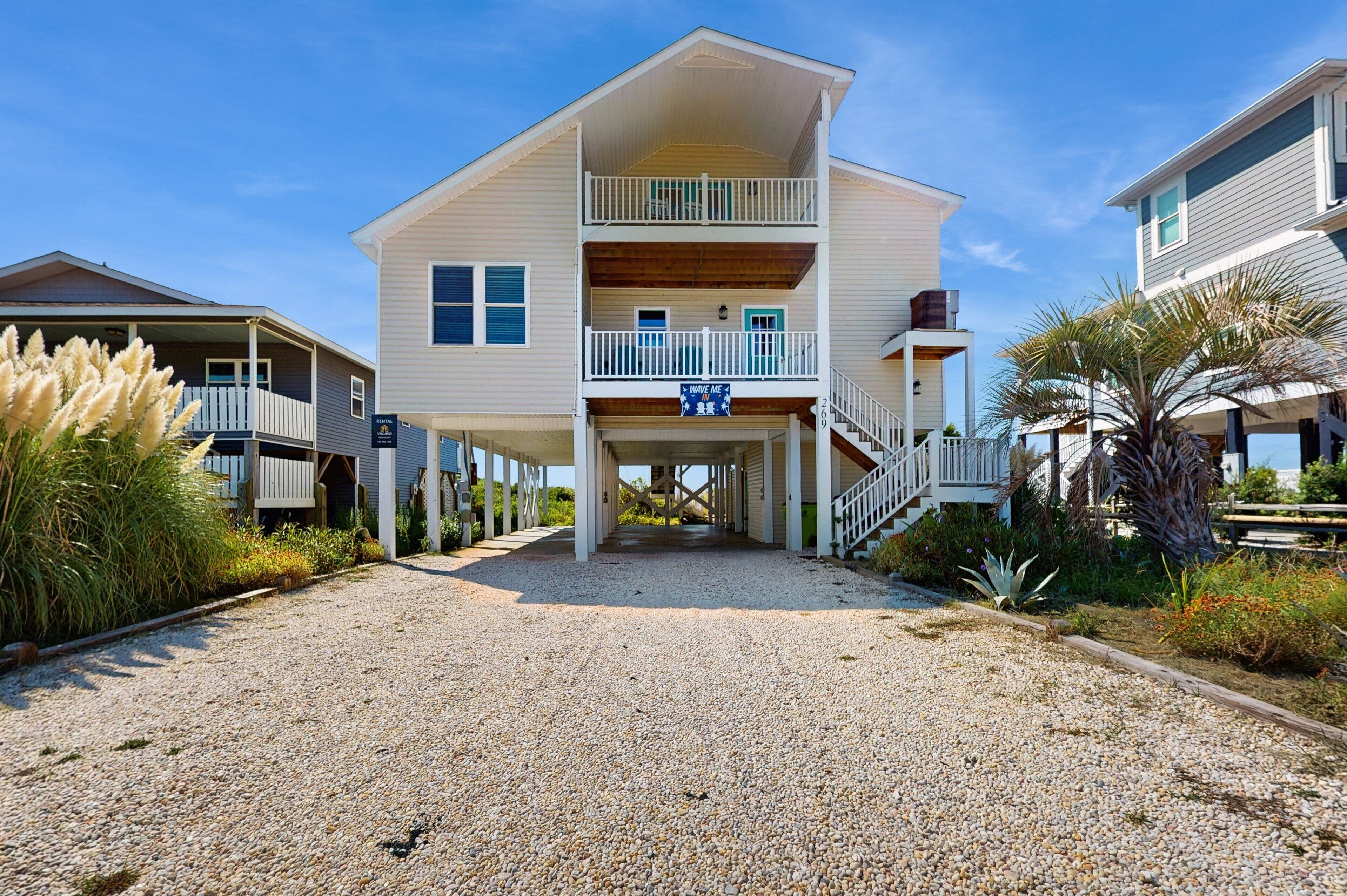 A two-story beachfront house with a covered porch, a balcony, and a sign that reads "Have a nice day."