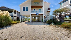 A two-story beachfront house with a covered porch, a balcony, and a sign that reads "Have a nice day."