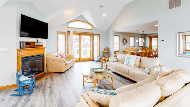 Ein geräumiges Wohnzimmer mit Kamin, Sofas, einem Fernseher und einem Essbereich mit Stühlen und Tisch.
