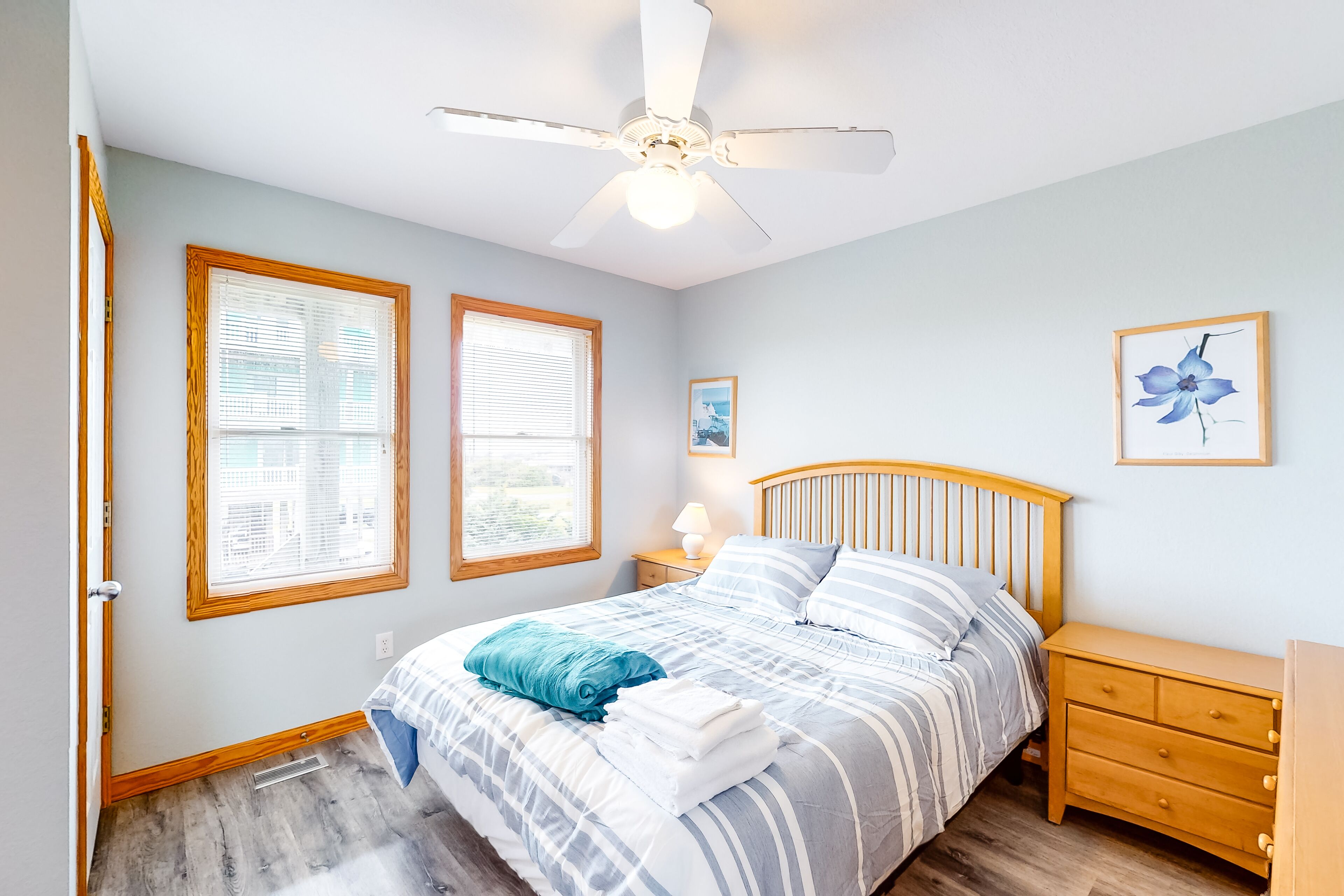 A bedroom with a bed, nightstands, a ceiling fan, and two windows.