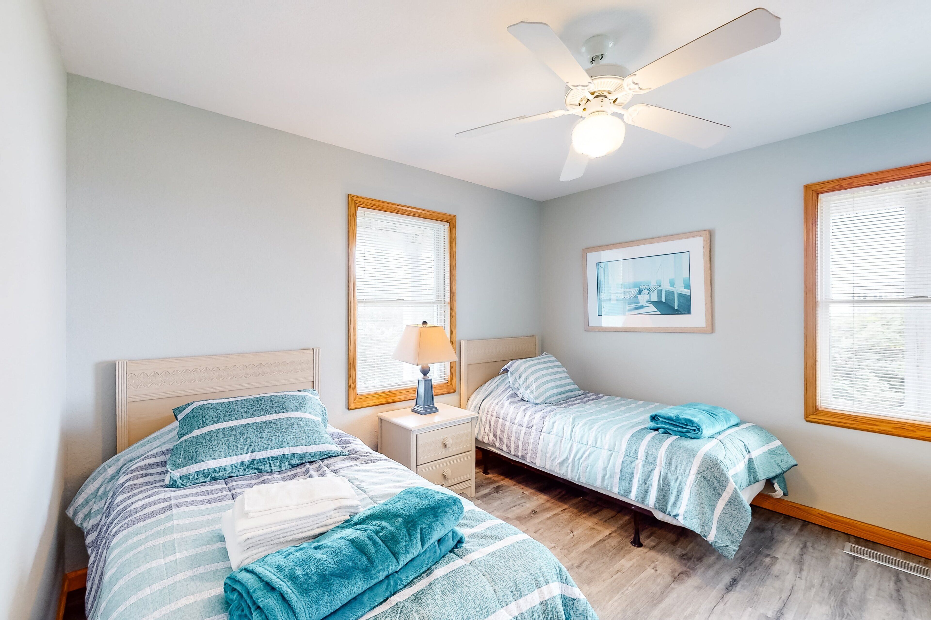A bedroom with two beds, a ceiling fan, and a window with blinds.