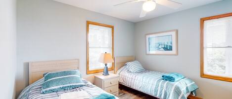 A bedroom with two beds, a ceiling fan, and a window with blinds.