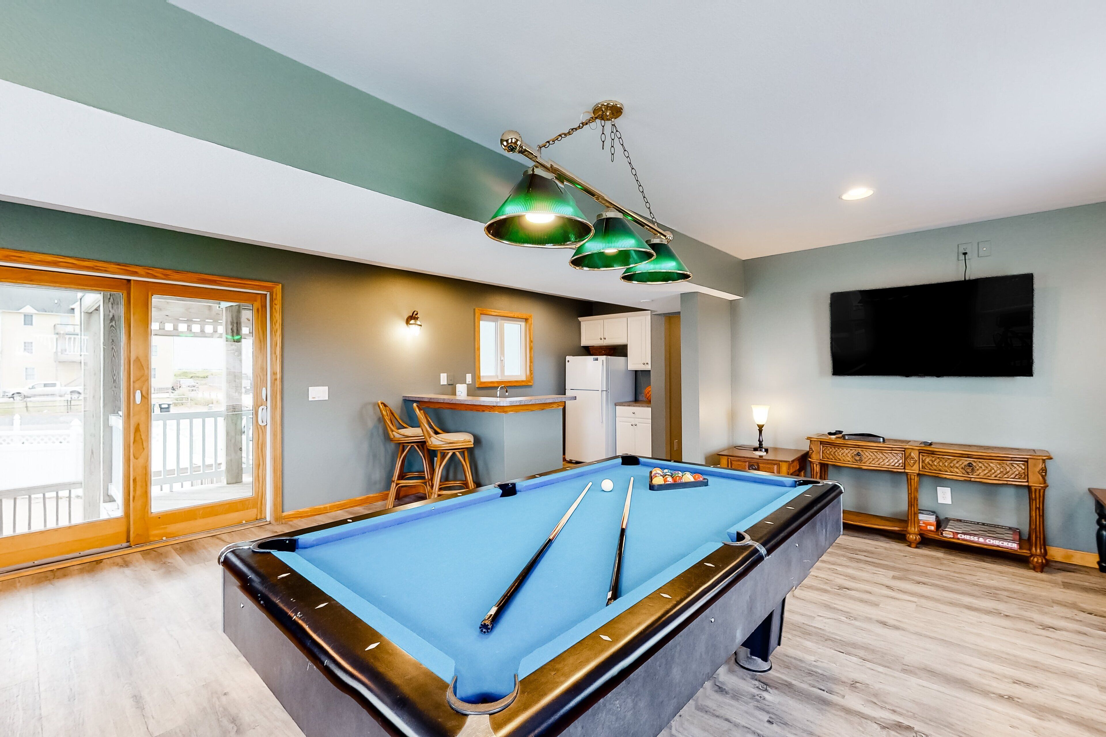 A pool table with cues, a television, and a small kitchen area with a sink and cabinets.