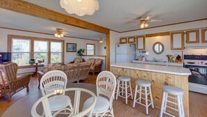 A spacious living room with wicker furniture, a kitchen with wooden cabinets, and a bar area with stools. - Oyster Cove 341: Cove-front, rooftop deck w/views, boat dock (Avon)