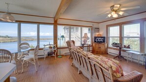 A spacious room with large windows overlooking a body of water, wicker furniture, and a ceiling fan. - Oyster Cove 341: Cove-front, rooftop deck w/views, boat dock (Avon)
