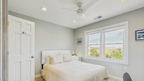 A bedroom with a bed, a nightstand, a chair, and a window with a view.