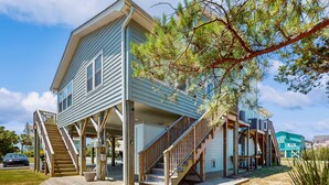 A two-story house with a wooden deck, a staircase, and a large tree in front.