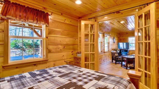 A cozy log cabin room with a large bed, a dining area, and a TV. - Free Ruby Falls Ticket & More -Hot tub-3 acres-5 min walk to lake fishing-15 min Cloudland Canyon (Rising Fawn)