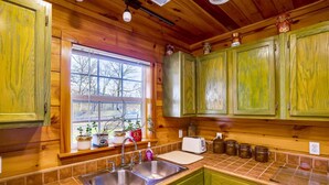 A kitchen with wooden cabinets, a sink, a window with plants, and a toaster. - Free Ruby Falls Ticket & More -Hot tub-3 acres-5 min walk to lake fishing-15 min Cloudland Canyon (Rising Fawn)