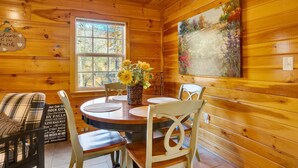 A wooden cabin interior with a round dining table, two chairs, a vase with sunflowers, a painting on the wall, and a welcome sign. - Free Ruby Falls Ticket & More -Hot tub-3 acres-5 min walk to lake fishing-15 min Cloudland Canyon (Rising Fawn)