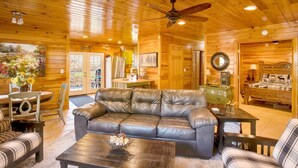 A cozy log cabin interior with a leather sofa, dining table, and a ceiling fan. - Free Ruby Falls Ticket & More -Hot tub-3 acres-5 min walk to lake fishing-15 min Cloudland Canyon (Rising Fawn)