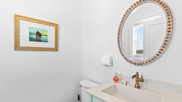 Een badkamer met een lijstfoto, een ronde spiegel, een wastafel en een toilet.