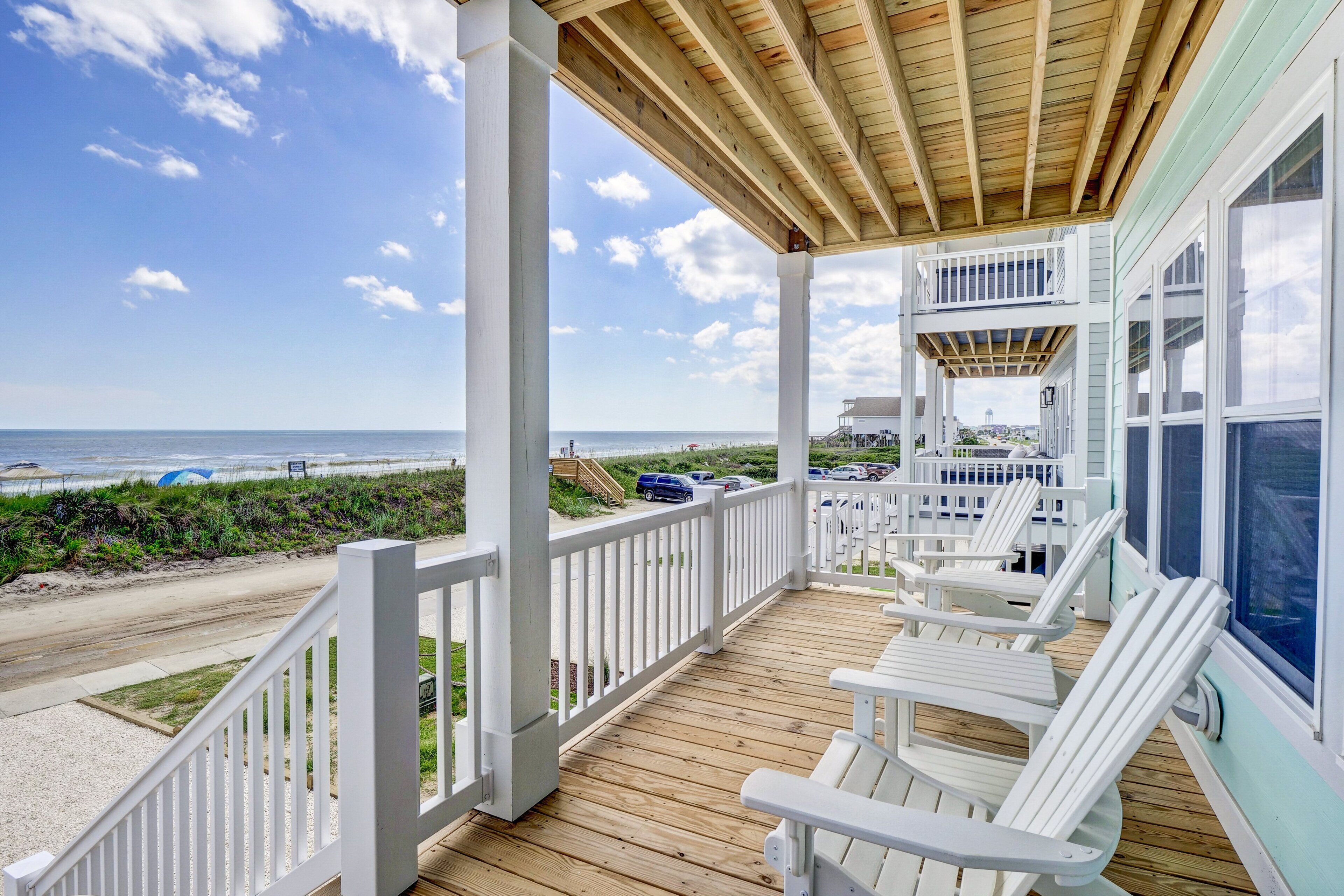 Une terrasse en bois avec des rampes blanches et des chaises longues donnant sur une plage.