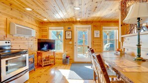 Interior acogedor de una cabaña con paredes y techo de madera, televisor, estufa y comedor.