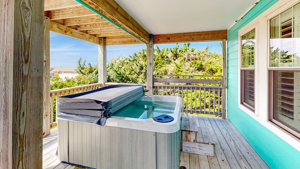 En træterrasse med jacuzzi, træværn og udsigt over grøn bevoksning.