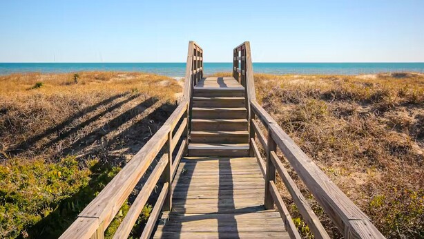 A wooden boardwalk leading to a beach with clear skies. - Condo near the beach with pool, BBQ area, balcony, & fireplace (Holden Beach)