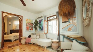 A cozy room with a bed, a sofa, a chair, a small table, and a large mirror. There is a window with curtains and a plant. - Casa Santorini: elegant stay next to La Ermita (Mérida)