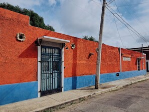Un edificio con fachada roja y base azul, que cuenta con una reja metálica y un ventanal pequeño.