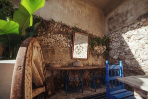Una habitación rústica con pared de piedra, una mesa de madera, una silla azul y una planta grande.