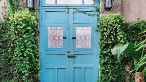 A blue door with glass panels, flanked by lush greenery and a concrete wall. - Casa Santorini: elegant stay next to La Ermita (Mérida)