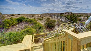 Un escalier en bois mène à une plage de sable où la végétation est clairsemée.