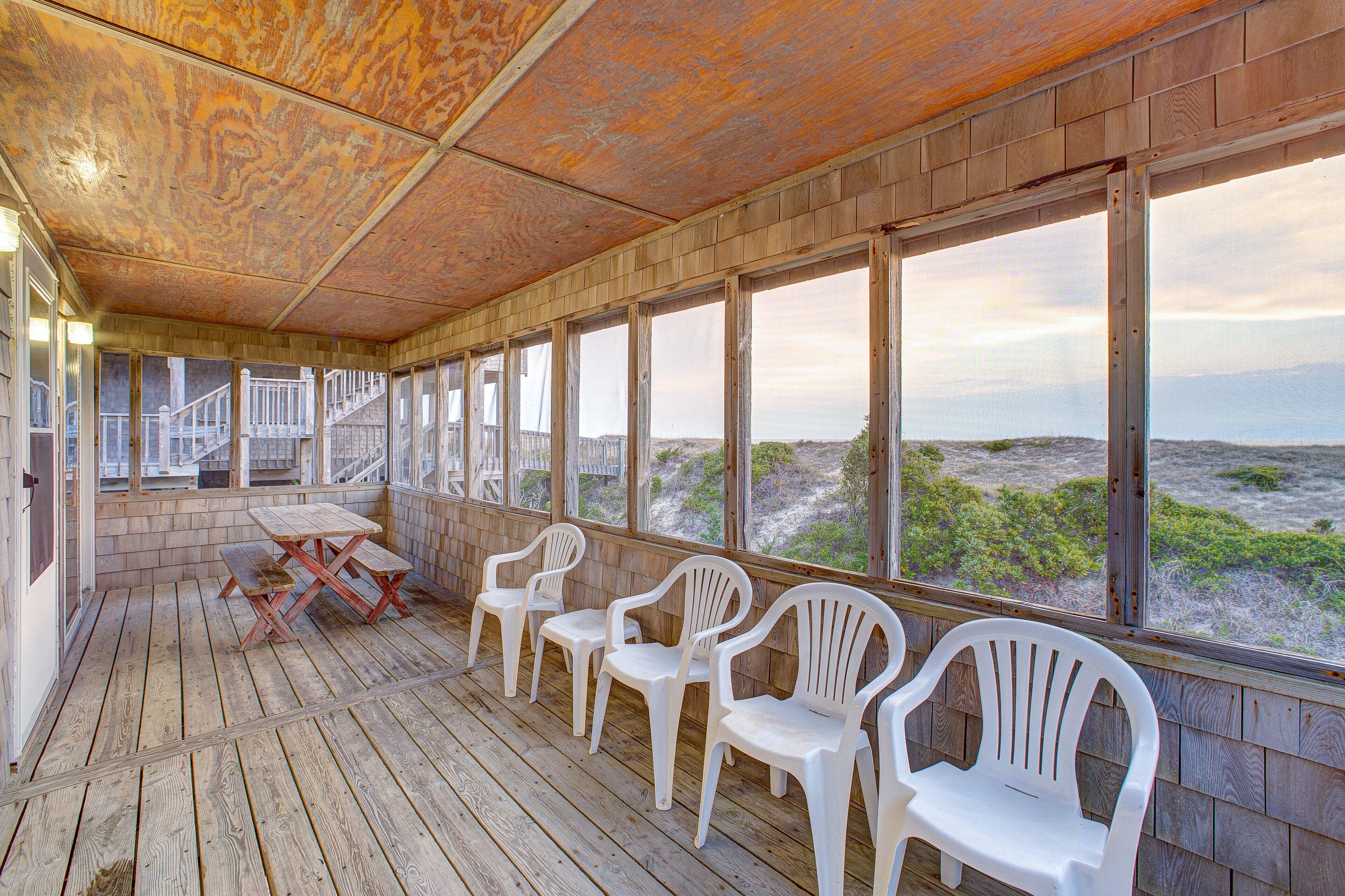 A covered outdoor area with wooden flooring, white plastic chairs, and a table.